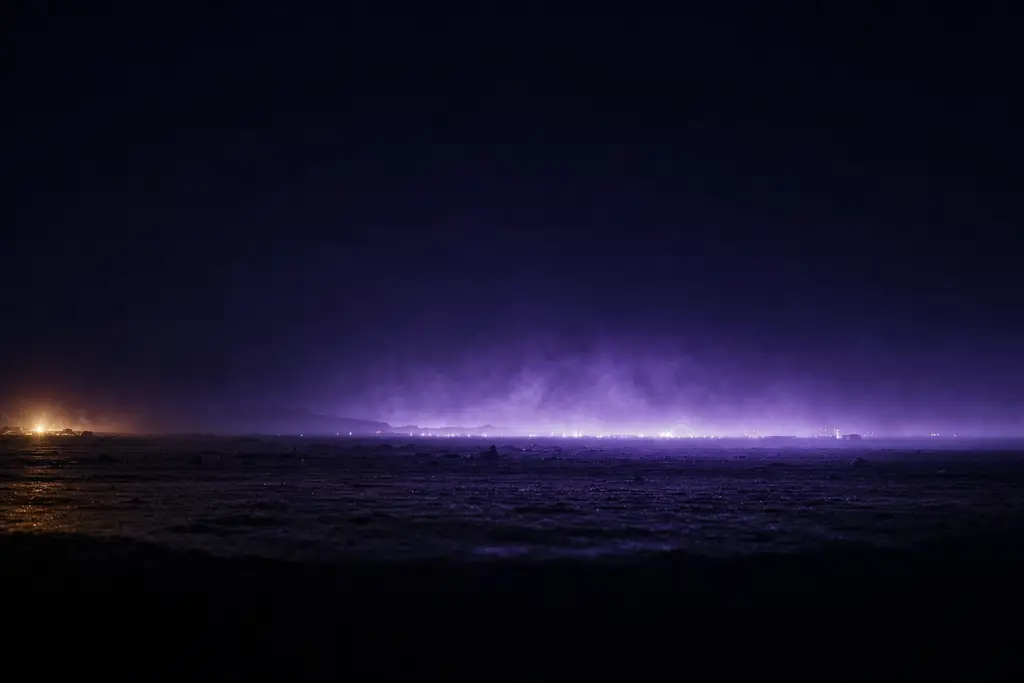 A wide dark horizon with a low band of violet light breaking across it and haze rising above.