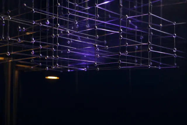 An abstract lattice of thin illuminated rods receding into darkness, suggesting structure and depth.