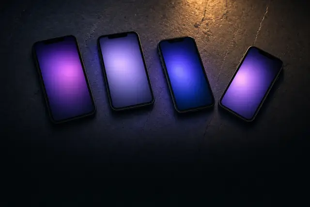 Several dark phone handsets arranged on a slate surface, each screen glowing a soft violet with no visible content.